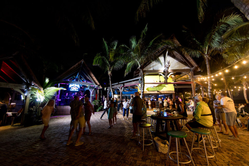 Night photo of the interior of the Square Grouper Tiki Bar on the Fort Pierce Inlet with a band on stage with patrons standing and at tables